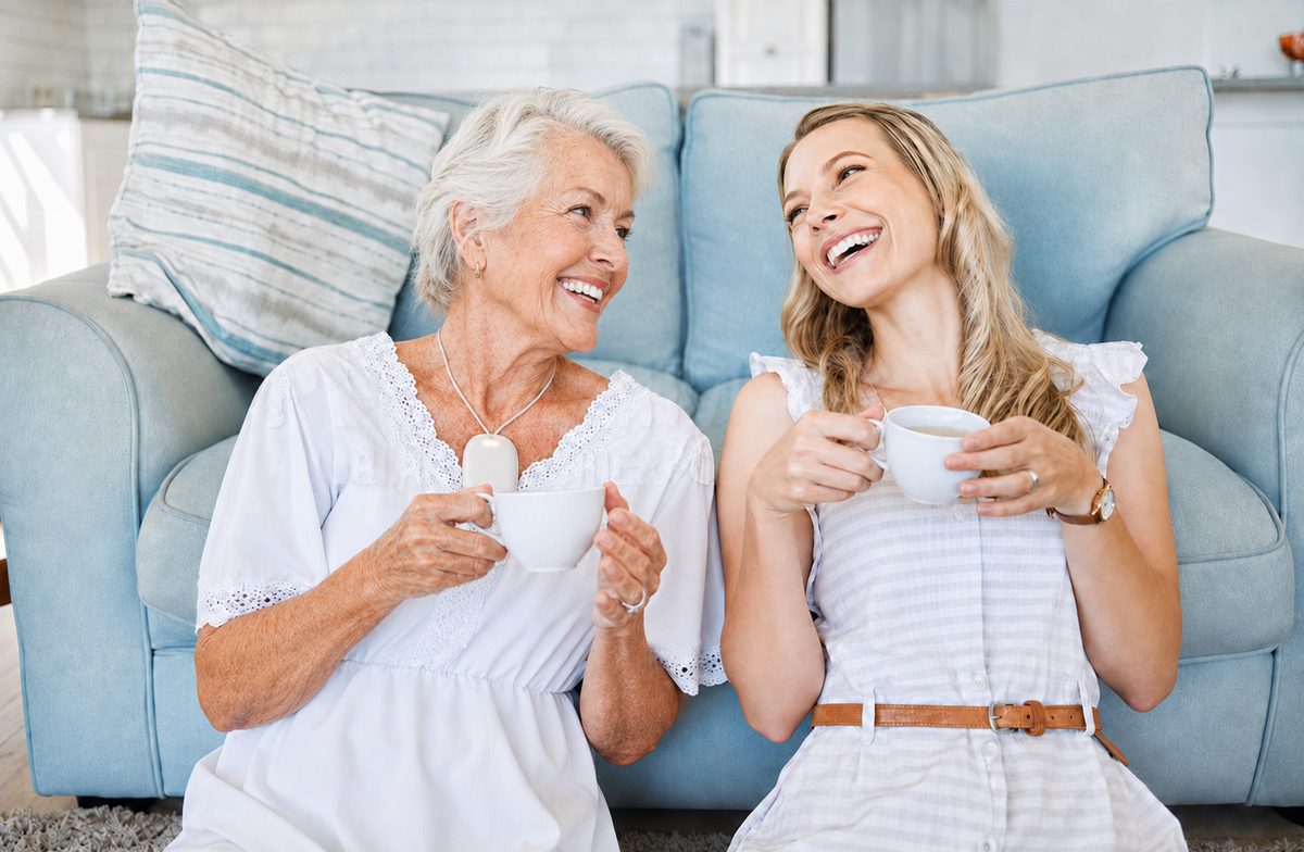 Margaret at home on the sofa with her daughter, laughing over tea and wearing her EvoCoach pendant.